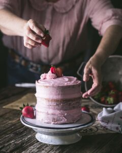 woman garnishing strawberry layer cake on a plate