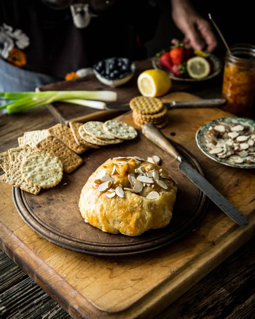 Whole baked brie on a cutting board with crackers