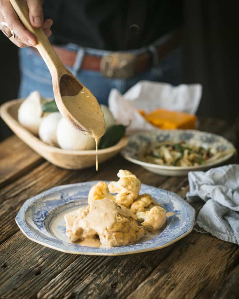 woman spooning cheese sauce over chicken