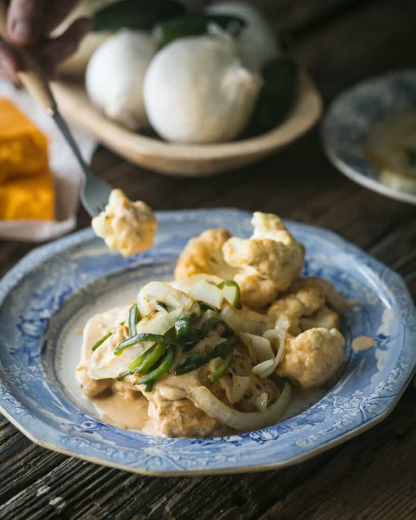 fork with morsel of cauliflower and serving of vegetable topped chicken