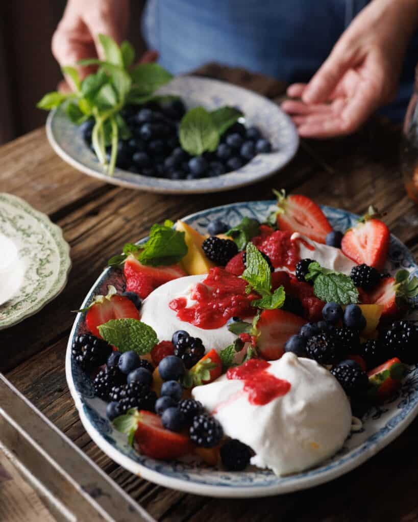 woman serving Summer Pavlovas with Honey Smashed Raspberries
