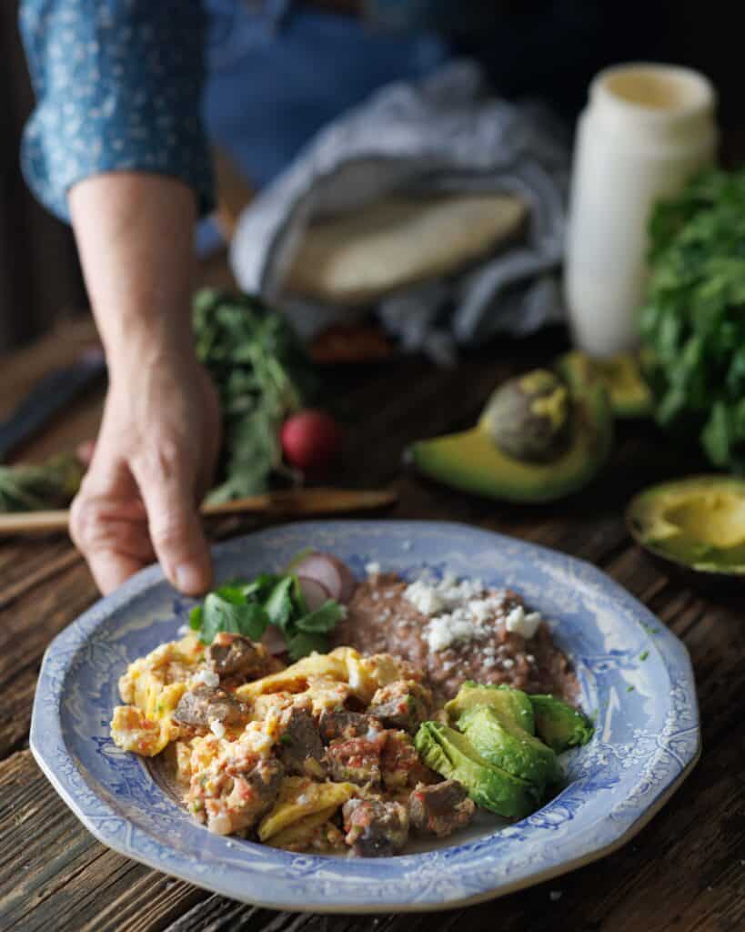 hand reaching out to plate of steak and eggs