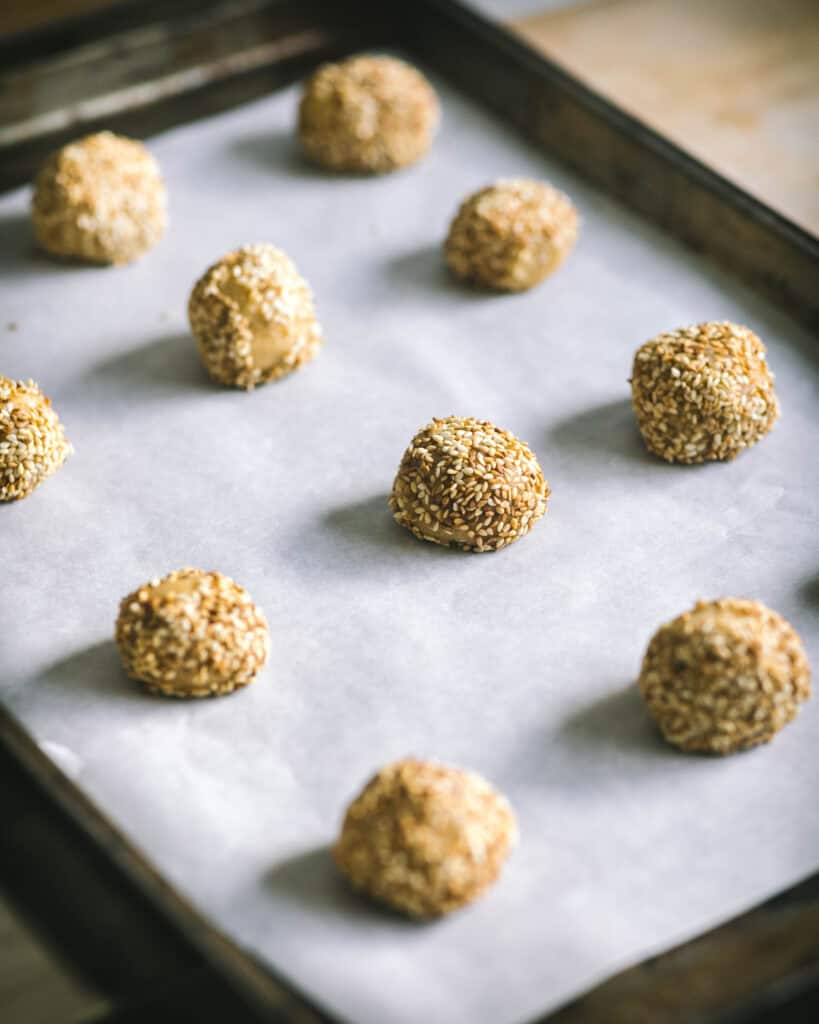 rolled balls of dough coated with sesame seeds on tray