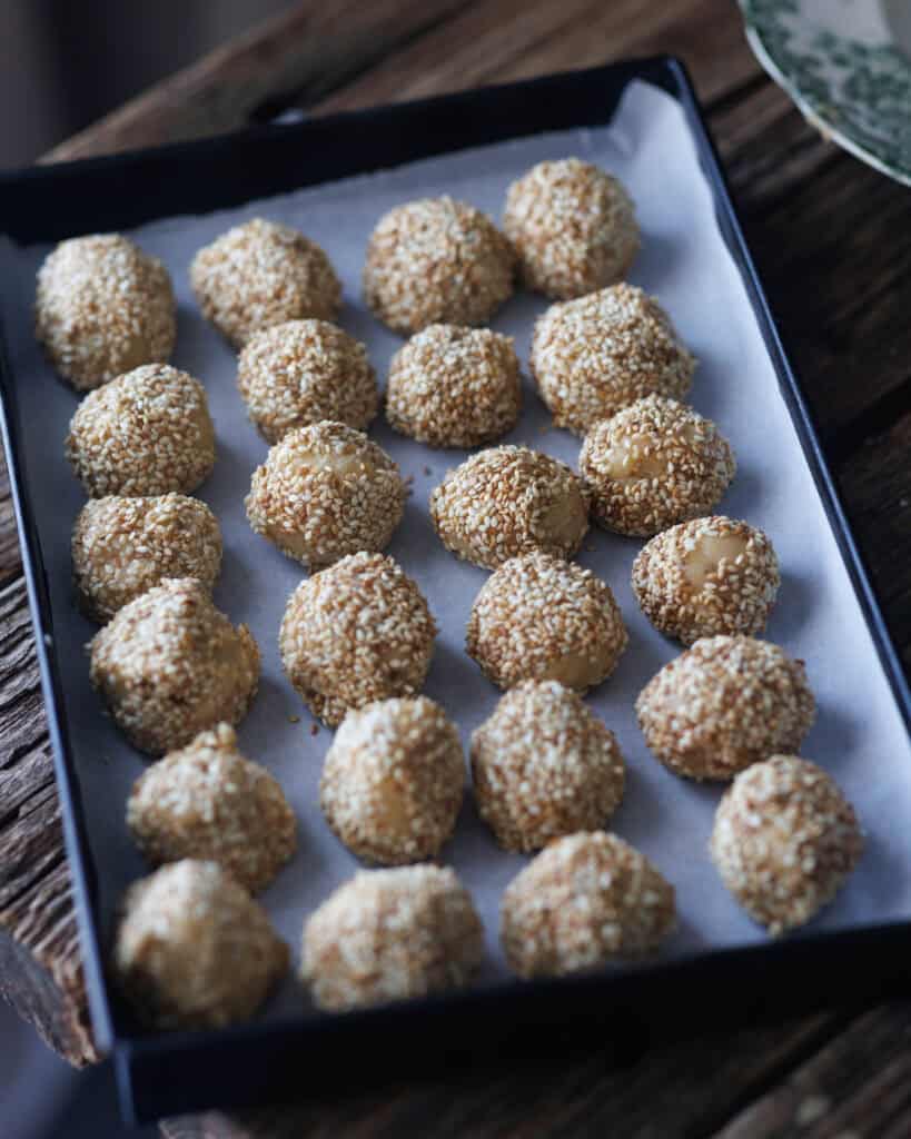 rolled balls of dough coated with sesame seeds on tray